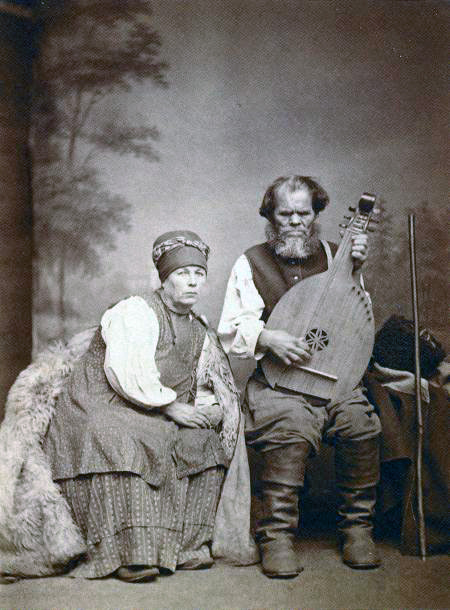 Kobzar Osip Veresai, aged, blind, sits next to his wife in his house, in his hands he has the national folk Ukrainian instrument - bandura, on which he plays. An old black-and-white photo from the 19th century.