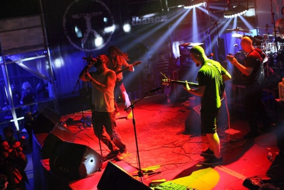 A high-octane metal band is rocking the stage, enveloped by a sea of colorful, flashing lights that pierce the dimly lit venue. The air is electric with excitement as the musicians deliver their ferocious sound, and the audience, lost in the music, pumps their fists and sways in unison. This scene encapsulates the fierce energy and vibrant atmosphere of a live concert, reminiscent of an exhilarating moment captured on video.
