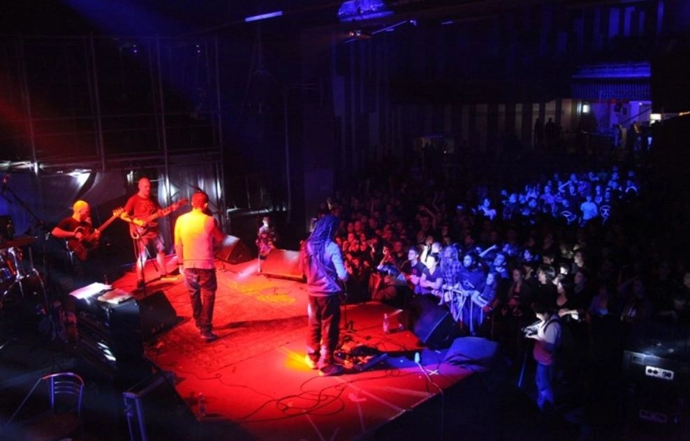 A fierce metal band commands the stage, bathed in a brilliant display of swirling lights that illuminate the shadowy surroundings. The atmosphere crackles with intensity as the musicians pour their energy into every note, while the audience responds with fervor, fists pumping and voices raised. This striking depiction captures the exhilarating spirit of a live show, akin to an electrifying snapshot from an iconic performance.