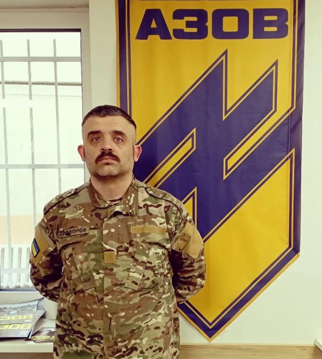 Vasil Pereverzev is in uniform. Photo of Ukrainian soldier under the banner of Azov unit in uniform. A famous Ukrainian rocker went to fight against Russian aggression. Strong, clear, bold and determined look, moustache.