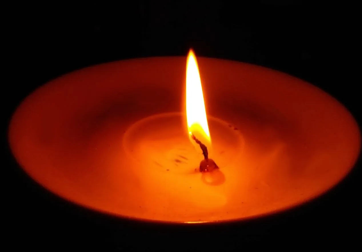 A single candle flame glowing brightly against the darkness, symbolizing hope and light in times of despair.